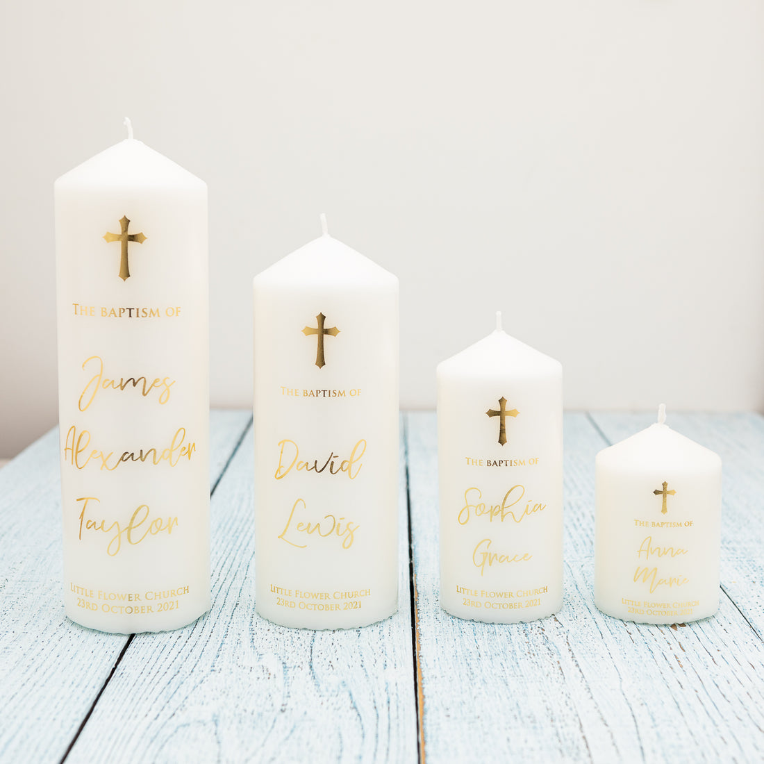 Four white candles in different sizes. All of them has the cross on top and the name of the person to be baptised together with the baptism date and the name of the church