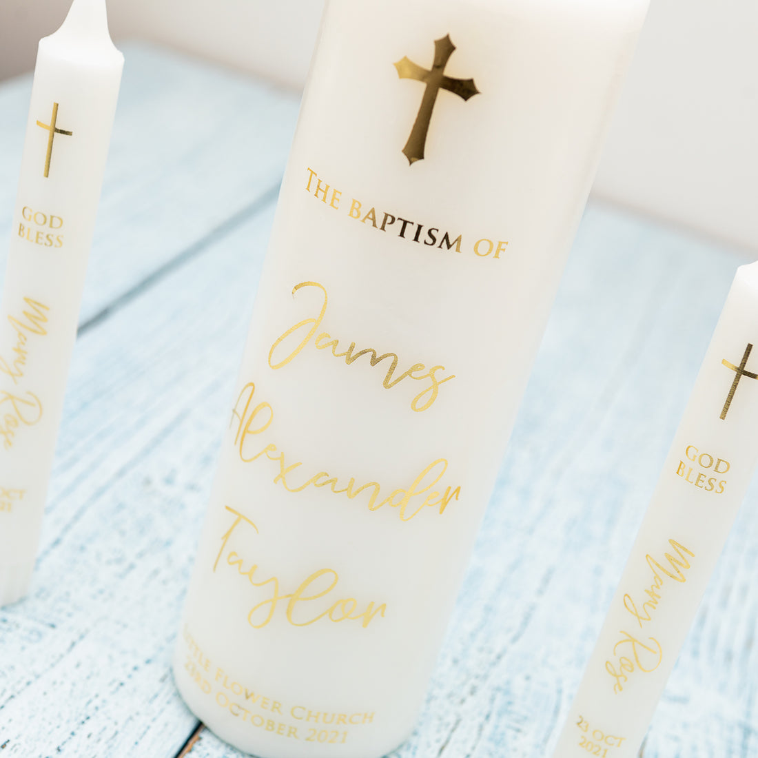 Four white candles in different sizes. All of them has the cross on top and the name of the person to be baptised together with the baptism date and the name of the church